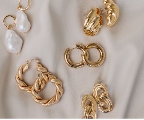 Flatlay med guldfärgade örhängen och ringar på ljust tyg